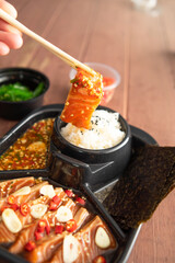 Salmon pickled in soy sauce or shoyu sauce and sprinkled with chili and sliced garlic. with spicy sauce Seaweed and Japanese rice are side dishes on a brown wooden table.