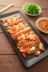 Salmon pickled in soy sauce or shoyu sauce and sprinkled with chili and sliced garlic. with spicy sauce Seaweed and Japanese rice are side dishes on a brown wooden table.