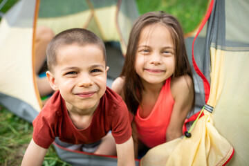 Fototapeta na wymiar Two little adorable kids smiling and looking out of tent in camp in forest in summer outdoors