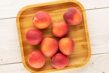 Several sweet red apricots with a bamboo tray on a wooden table, close-up, top view.