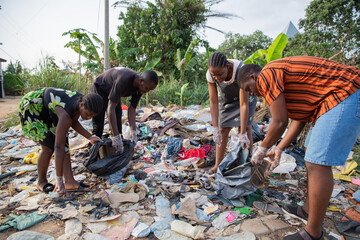 Four young adults collect garbage in an illegal open-air landfill in africa, people against...