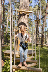 Obraz premium Happy child, school girl enjoying activity in a climbing adventure park on a summer day.