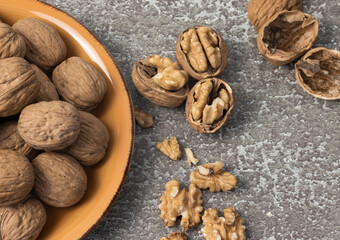 Plate with whole walnuts and shells on wooden table