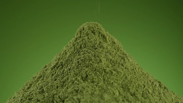 Pouring green superfoods powder close up. Matcha green tea or Chlorella or spirulina powder on green background