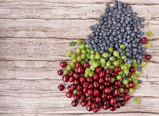 Texture of ripe blueberries, gooseberries and cherries on a wooden table. Flat lay on a background of seasonal berries