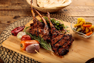 Lamb Chops with pickle and bread served in a wooden cutting board isolated on wooden background...