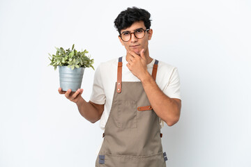 Gardener Argentinian man holding a plant isolated on white background thinking