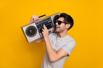 Photo of funky brunet millennial guy hold look boombox wear t-shirt glasses isolated on yellow...