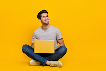 Full length photo of boss brunet millennial guy sit with laptop look promo wear t-shirt jeans shoes isolated on yellow background