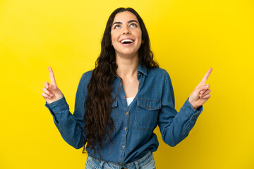 Young caucasian woman isolated on yellow background surprised and pointing up