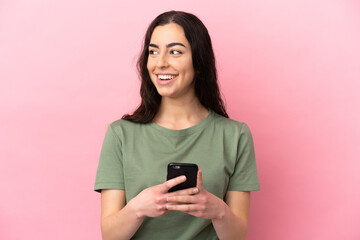 Young caucasian woman isolated on pink background using mobile phone and looking up