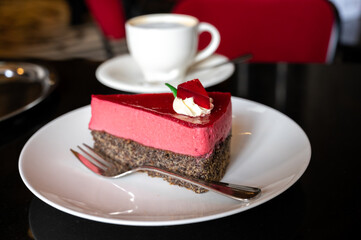 Piece of famous Poppy seed cake with raspberry mousse of Austrian origin served with whipped cream and cup of coffee