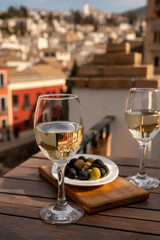 Two glasses of Spanish dry rueda white wine served with olives on roof terrace with view on old part of Andalusian town Granada, Spain