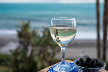 Hand with glass of Spanish dry white wine on beach terrace with view on Mediterranean sea