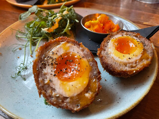 two scotch eggs on a white pale with garnishing.