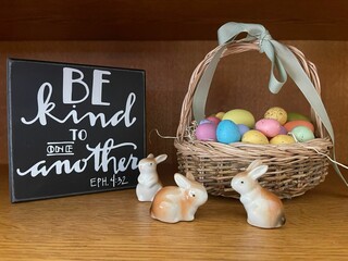 Closeup of a basket with Easter eggs and an art stencil with a quote and porcelain rabbit figurines