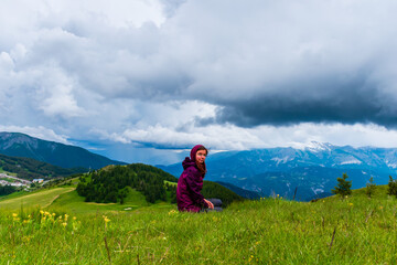 Obraz premium A wide angle shot of a young female hiker on a break during a hike on a cloudy summer day in the French Alps (Valberg, Alpes-Maritimes, France)