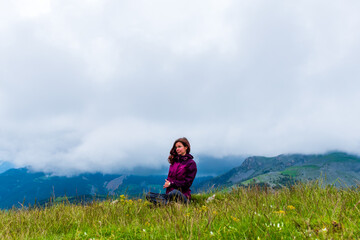 Naklejka na ściany i meble A wide angle shot of a young female hiker on a break during a hike on a cloudy summer day in the French Alps (Valberg, Alpes-Maritimes, France)