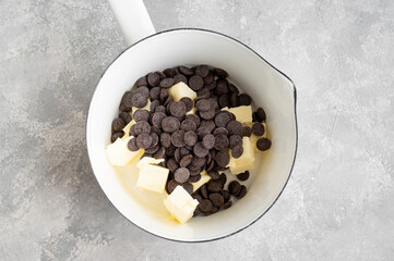 Melting dark chocolate drops and butter in a white saucepan on the table. The process of making glazed, chocolate cake, lava cake. Top view.