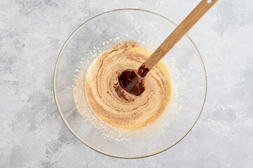 Raw beaten eggs with sugar and melted chocolate in a glass bowl on a gray concrete background. Preparation of cream, desserts, brownie, lava cake. Top view.