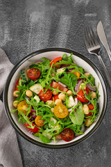 Salad with chickpeas, green leaves and fresh vegetables in a bowl on a gray concrete background. Healthy food. Top view, copy space.