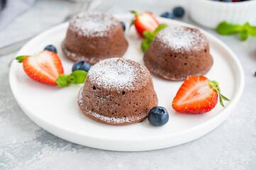 Chocolate fondant lava cake with fresh berries on a plate on a gray background.