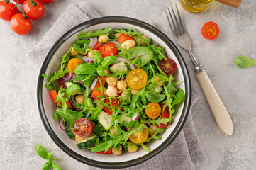 Salad with chickpeas, green leaves and fresh vegetables in a bowl on a gray concrete background. Healthy food. Top view, copy space.