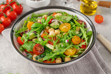 Salad with chickpeas, green leaves and fresh vegetables in a bowl on a gray concrete background. Healthy food. Top view, copy space.