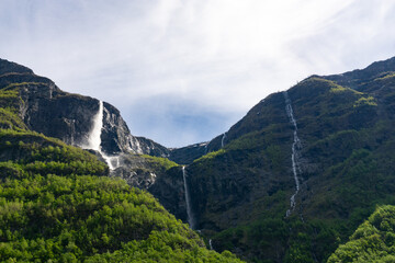 Fototapeta na wymiar Large waterfall that rises in the mountains surrounded by green trees in Norway.