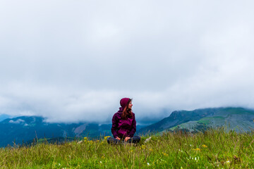 A wide angle shot of a young female hiker on a break during a hike on a cloudy summer day in the French Alps (Valberg, Alpes-Maritimes, France)