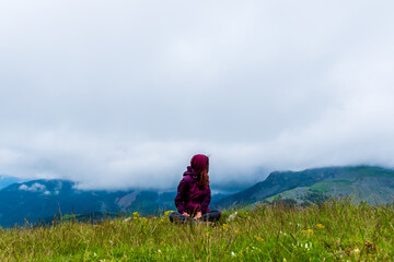 A wide angle shot of a young female hiker on a break during a hike on a cloudy summer day in the French Alps (Valberg, Alpes-Maritimes, France)