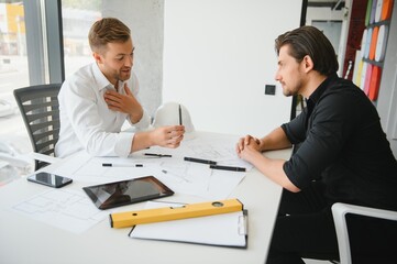 two people sit in front of construction plan and talk about the architecture