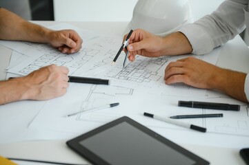Two young architects with blueprints of a house standing in office, talking.