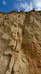 Ruined clay slope on the coast. Cracked clay cliff on the coast. A crumbling and cracked clay wall.
