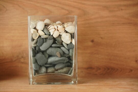 Closeup of a glass of seashells and pebbles on a wooden background
