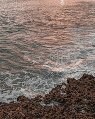 Vertical shot of sea waves hitting a rocky coast during golden hour