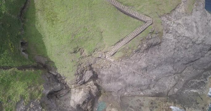 Drone footage of a rocky shore with a narrow staircase between the road and ocean in Philippines