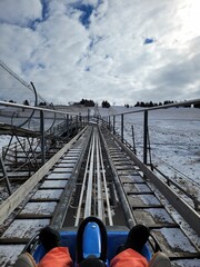 Vertical shot of a person sitting on an alpine coaster under a cloudy blue sky in winter