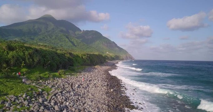 Drone shot of the sea with a forest on beach of Basco Batanes and a mountain covered with green