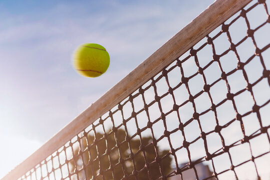 Tennis ball flies close over net, dangerous hit, ball is in motion, view from below.