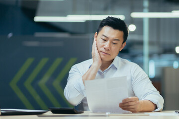 Portrait of a worried young businessman, accountant, financier. He sits at a desk in a modern...