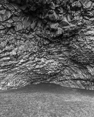 Vertical black and white shot of a cave on the beach with basalt stone walls in Iceland