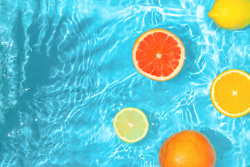 Refreshing sunny fruit scene with sliced citrus fruits and agitated blue water. Real summer nature. Creative copy space.