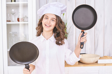 Young girl cooking at kitchen with pan. Curly pretty child portrait. Chef christmas student. Attractive brunette. Children emotion. People baking in cook apron. Close recipe menu - Powered by Adobe