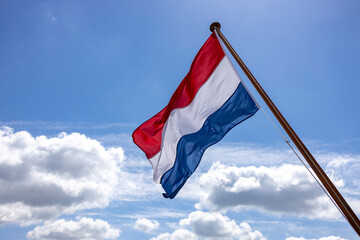 Clouds and blue sky framing tricolor of Dutch national flag blowing in a strong wind with texture...