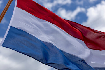 Naklejka premium Brightly lit tricolor of Dutch national flag blowing in a strong wind with texture and detail in the folds against a blue sky with clouds