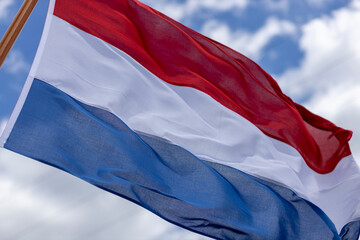 Intrinsic folds in tricolor of Dutch national flag blowing in a strong wind with texture and detail against a blue sky with clouds