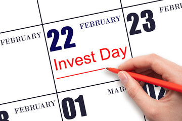 Hand drawing red line and writing the text Invest Day on calendar date February 22. Business and financial concept.