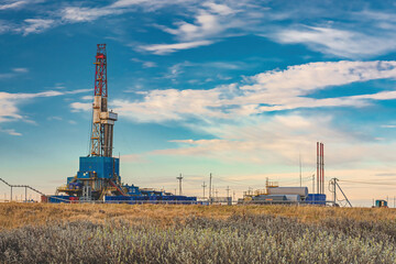 Fototapeta na wymiar The spring landscape of the Arctic tundra against the background of infrastructure for drilling wells and oil and gas production. In the foreground thickets of northern shrubs