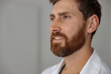 Obraz premium Close up of handsome doctor in uniform standing in medicine clinic hall and looking away